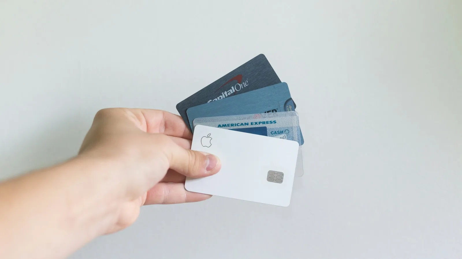 A hand holding several payment cards against a plain background