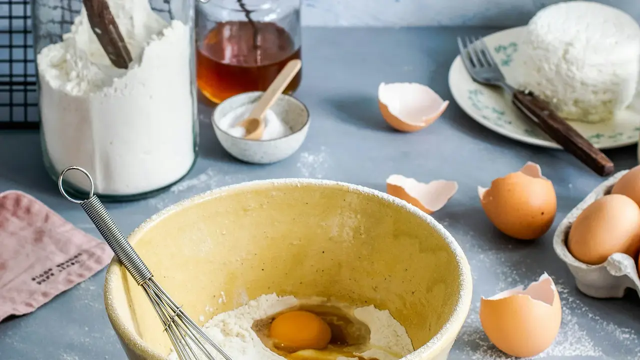 A mixing bowl with flour, eggs, and a whisk for baking