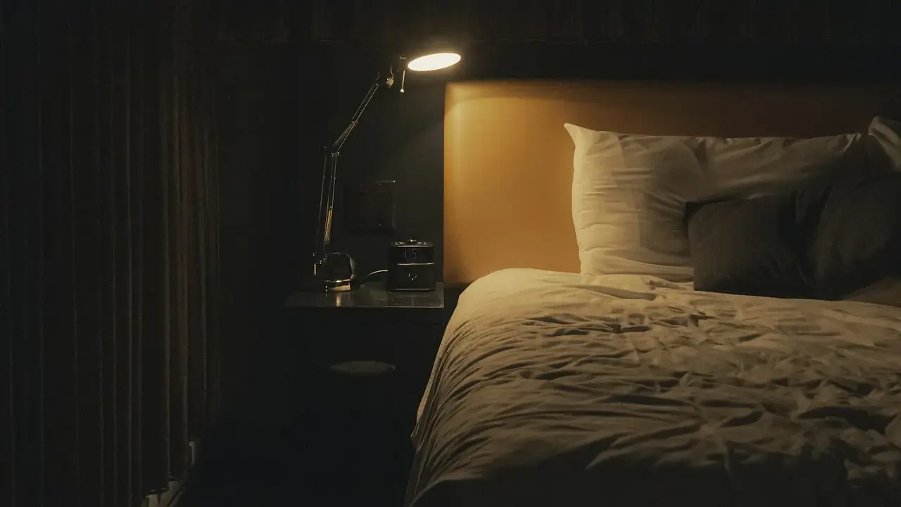 A warmly lit bedside lamp beside a neatly made bed