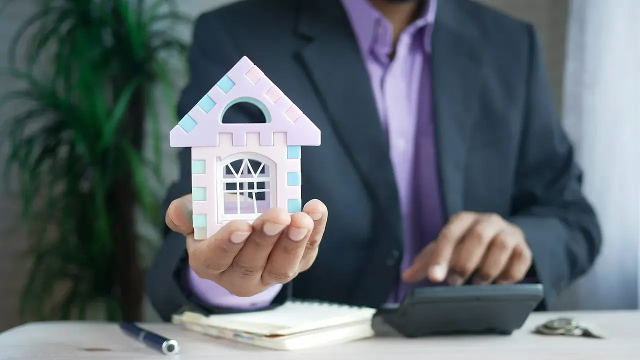 A person holding a model house beside mortgage calculations