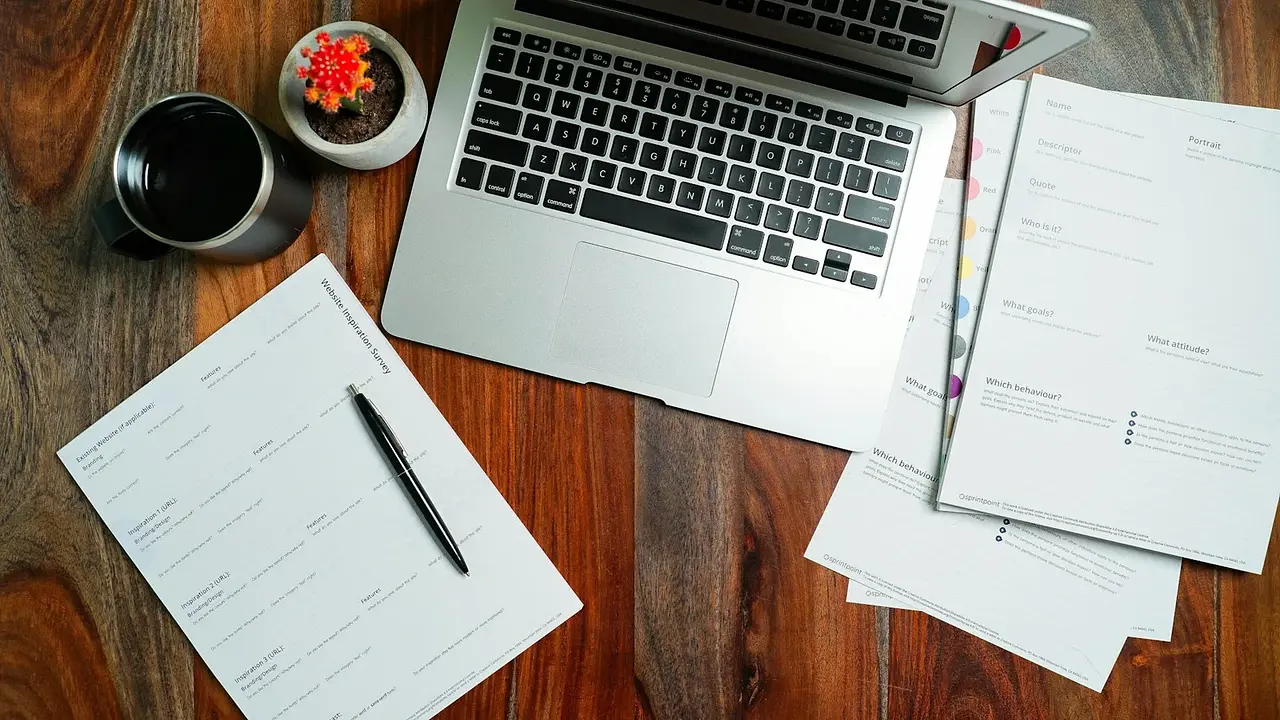 A laptop, notebook, and printed documents on a wooden desk