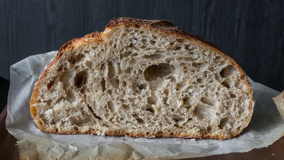 Sliced sourdough loaf with an open crumb on parchment paper atop a wooden table